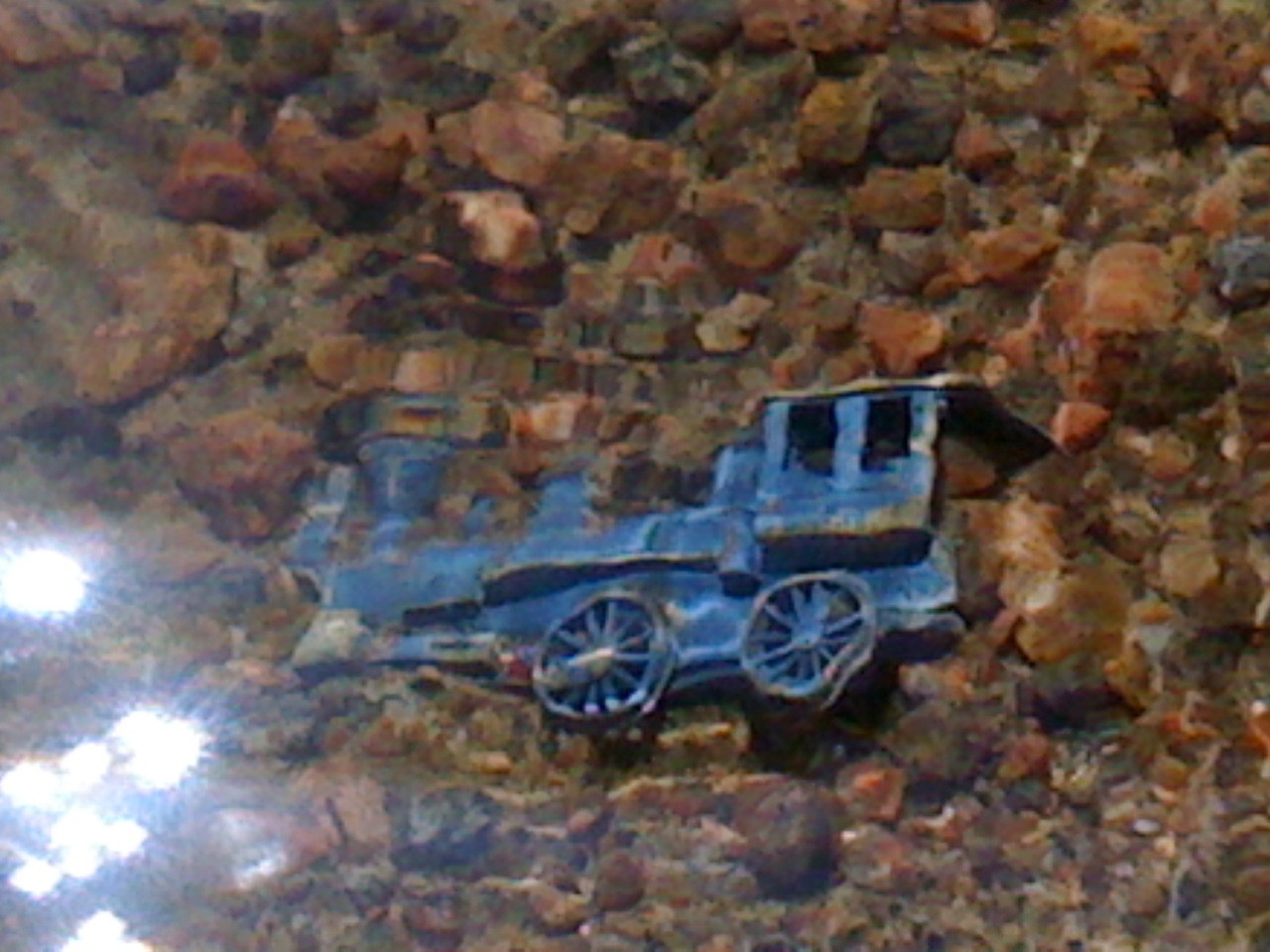 a Blue metal train locomotive rests on the rocks in shallow water half buried in sand