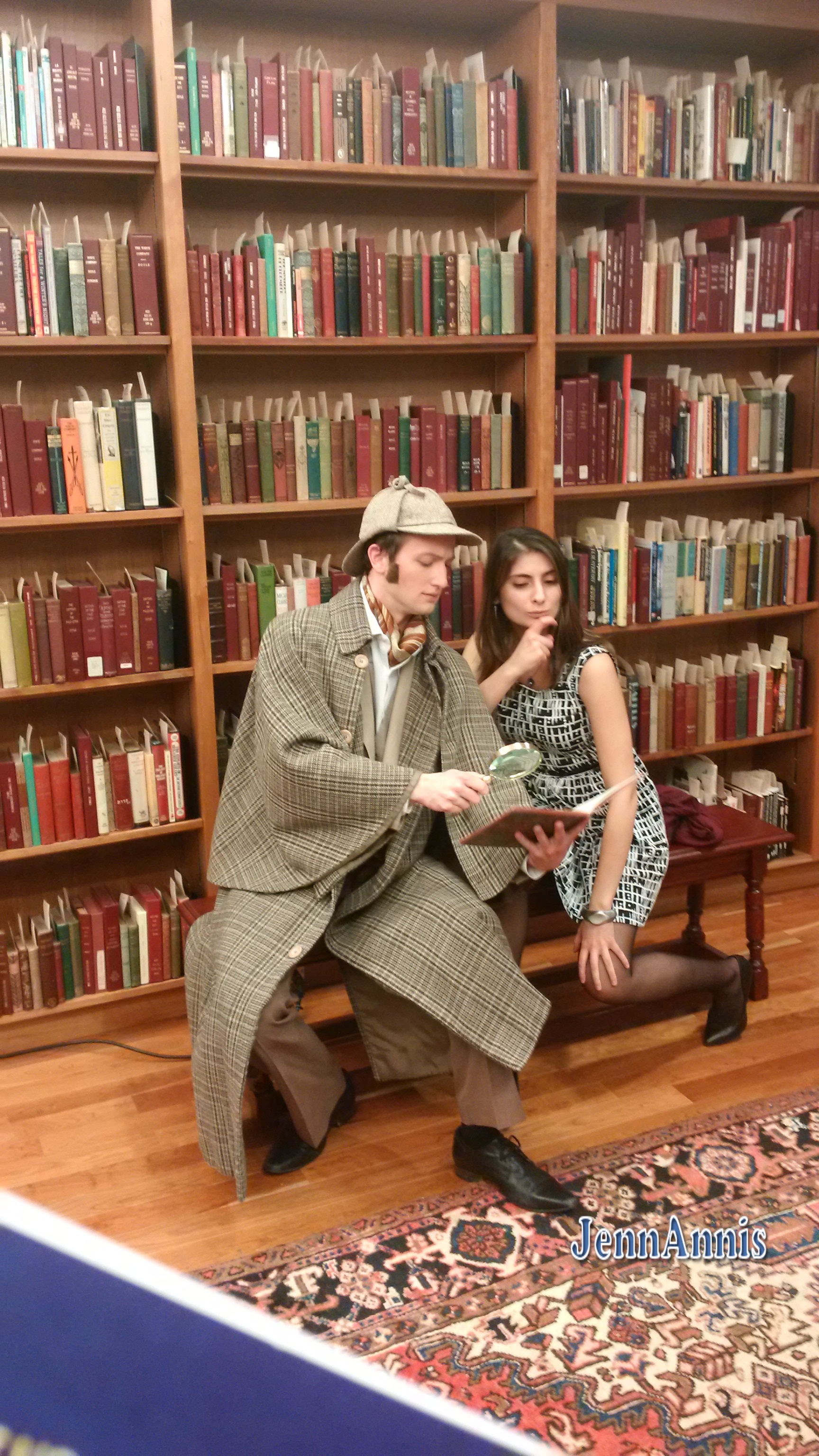 A man dressed as Sherlock Holmes in a tan cape and deerstalker hat poses in front of shelves full of books with a young woman