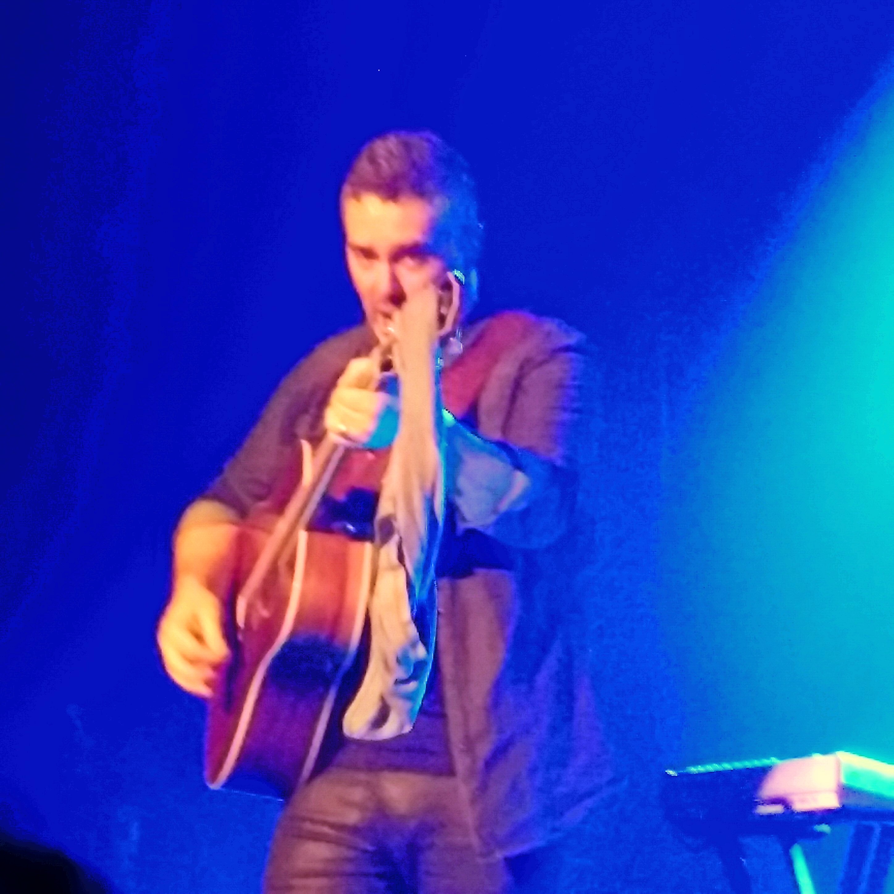 Ed Robertson points the guitar with the underwear still on it at the camera, smiling
