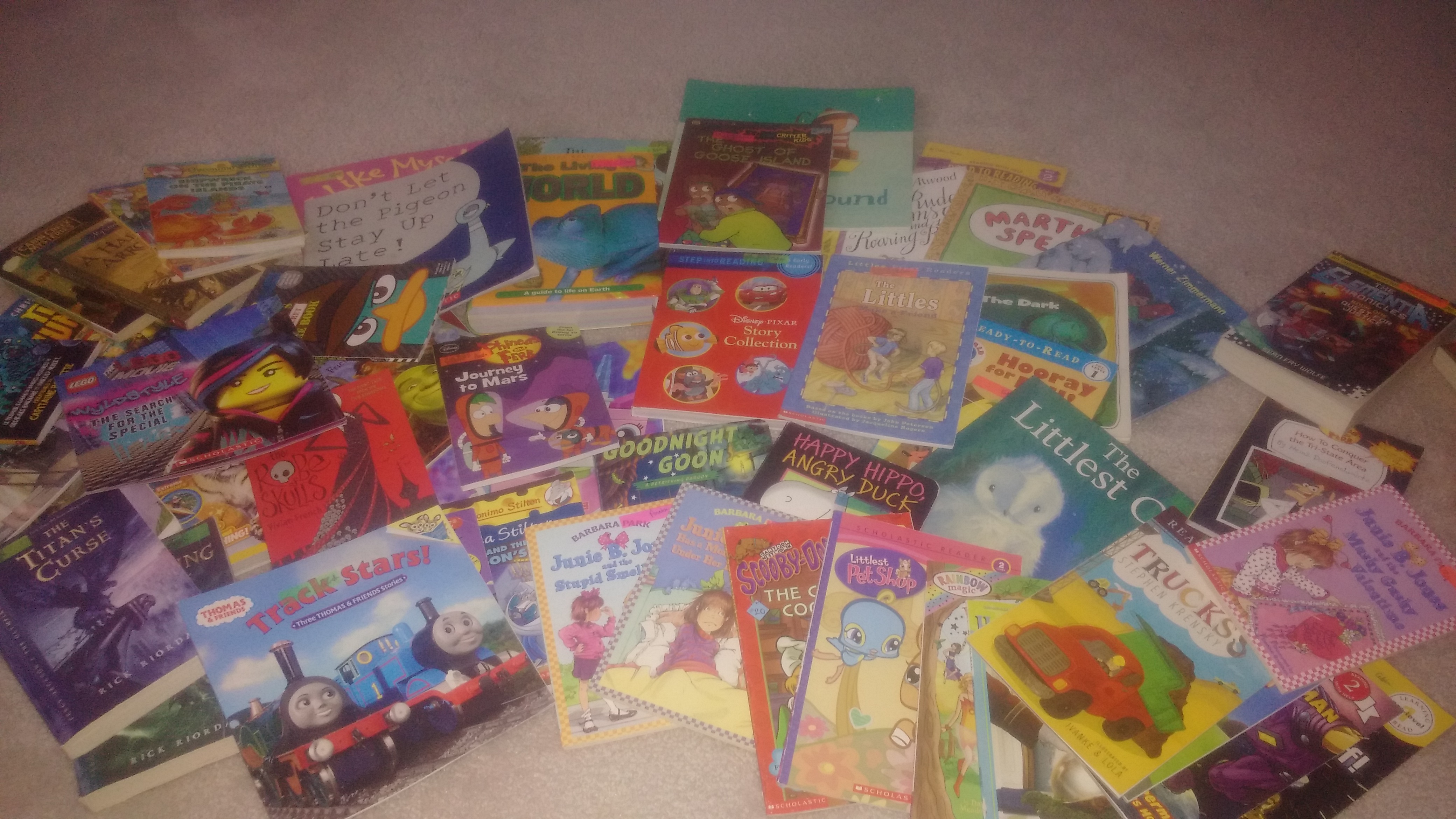 Around 30 picture books and early readers with a few young adult novels lie in a pile on the floor