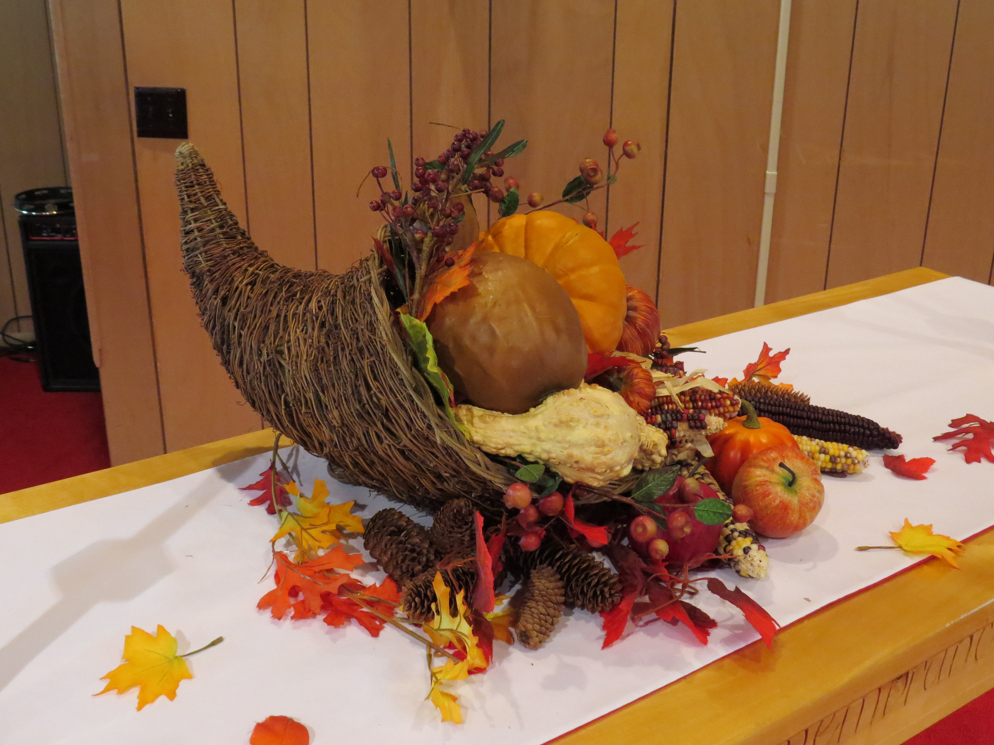 A wicker horn filled with gourds and pumpkin on a table with fake orange leaves around it