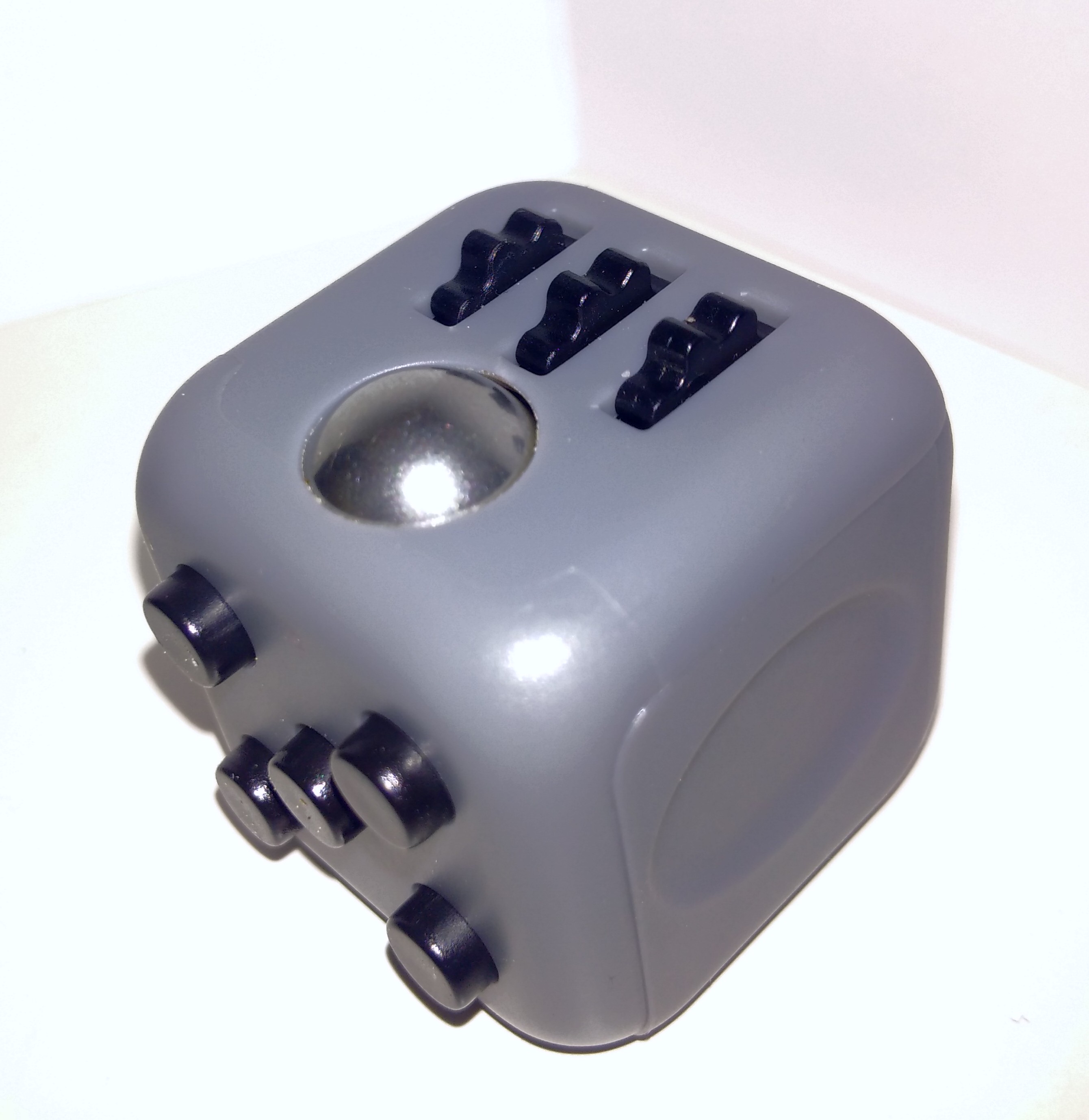 a grey plastic cube with buttons on one face, a smooth indent on another and a silver ball with 3 click wheels on the 3rd face you can see